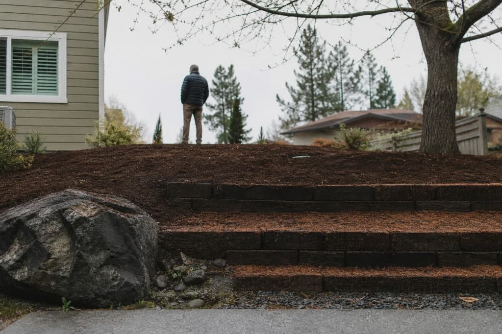 Mulched slope with stone steppers and shrubs on a residential lot.